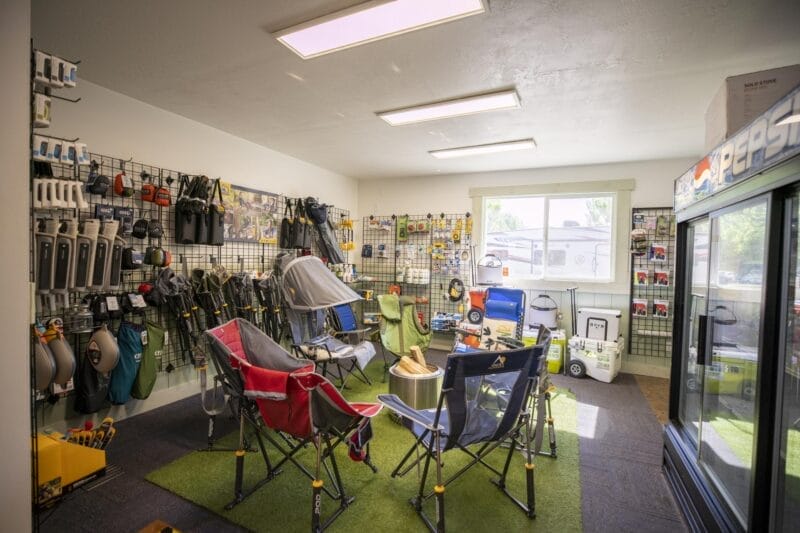 A small store showcases outdoor and camping gear, including folding chairs, coolers, tools, and accessories displayed on racks and shelves.