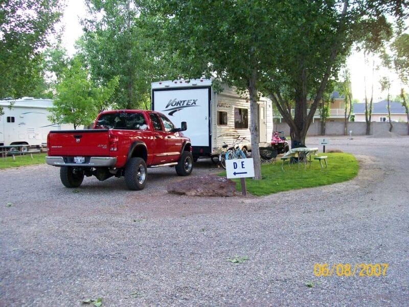 A red pickup truck and a Vortex travel trailer are parked at a campsite with a small grassy area, folding chairs, a table, and a sign labeled "DE". Date stamp: 06/08/2007.
