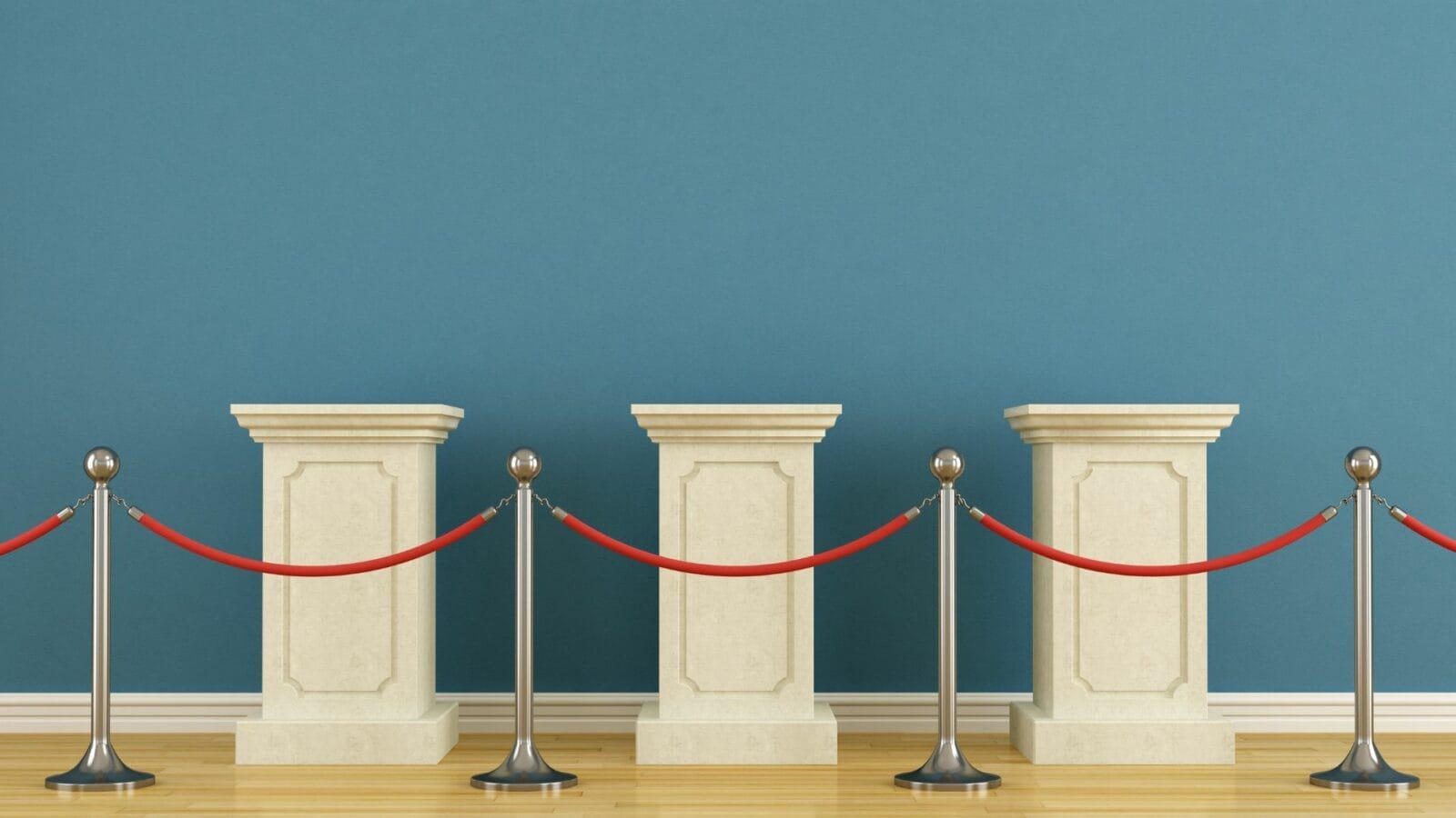Three empty stone display pedestals are positioned against a blue wall, separated by red ropes attached to metal stanchions on a wooden floor.