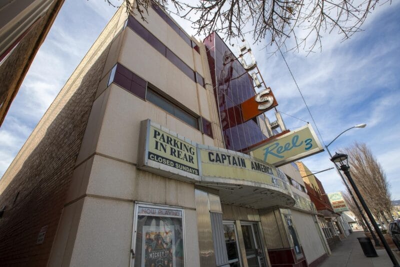 A vintage movie theater with a marquee advertising "Captain America" and "Reel 3," and a sign indicating parking in the rear. The building has a retro facade with red and beige panels.