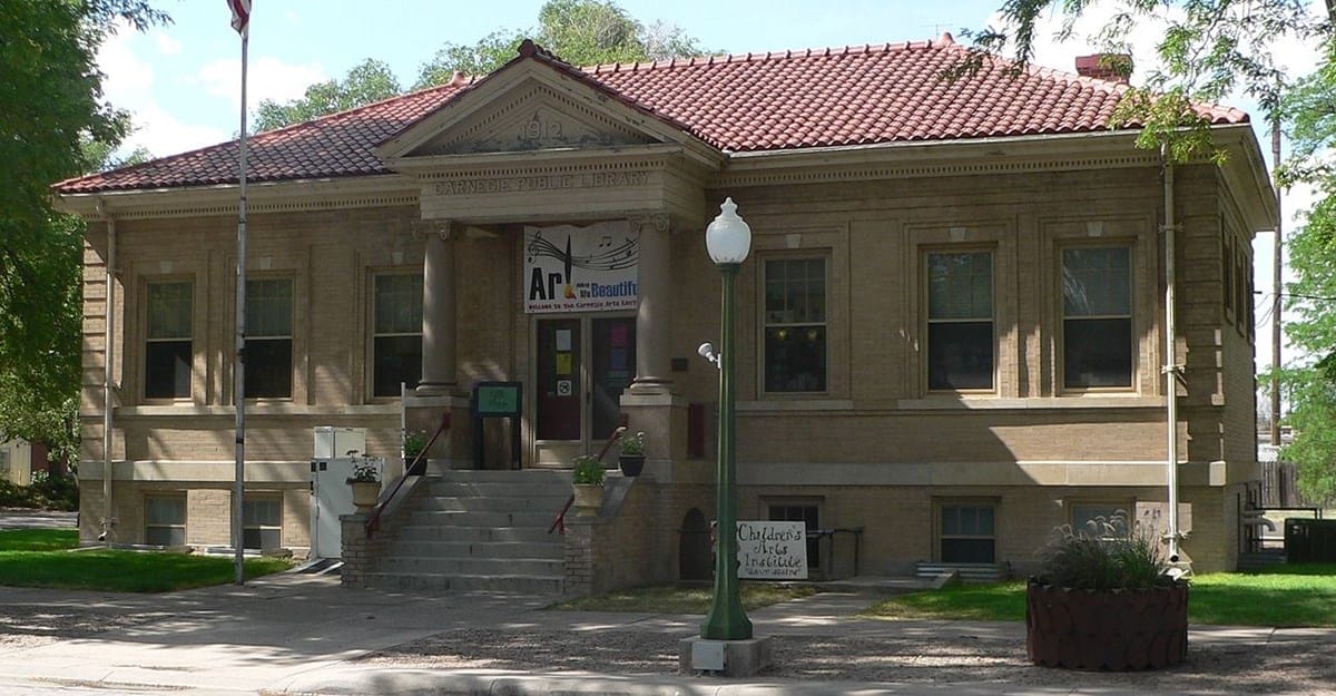 A historic brick building with a red tile roof, front steps, columns, and signage for an art museum, under a clear sky with surrounding trees.