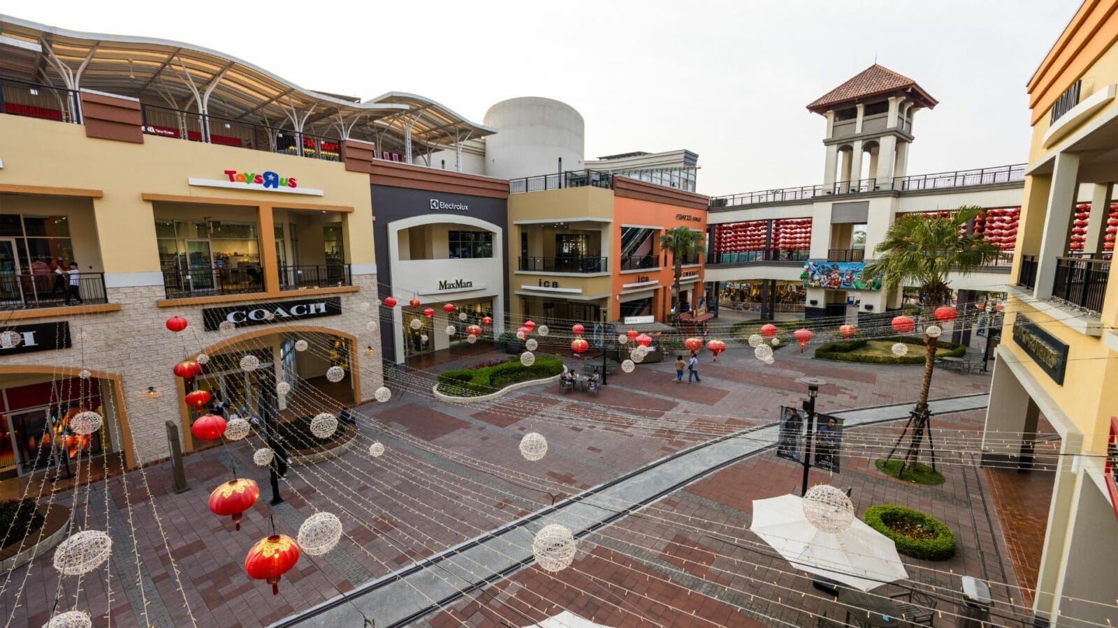 An outdoor shopping center with various retail stores, including Coach and Toys“R”Us, decorated with red lanterns and string lights.