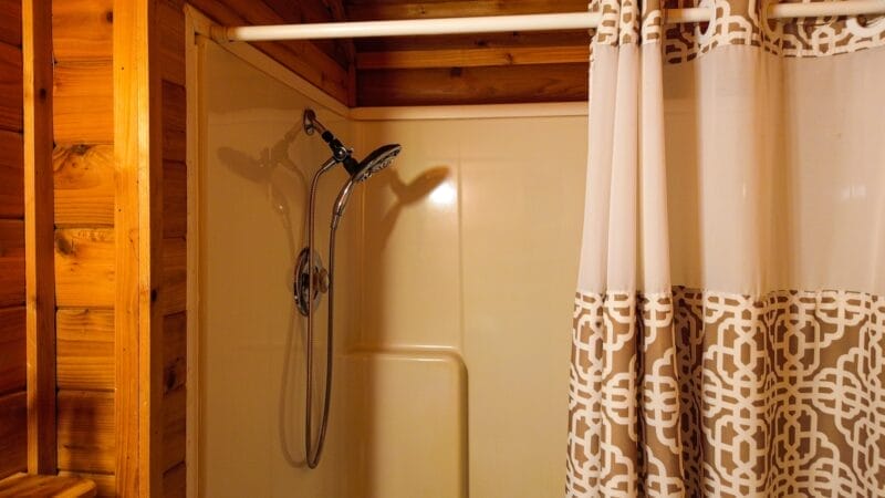 A shower with a handheld showerhead, cream-colored walls, and a patterned shower curtain in a wood-paneled bathroom.