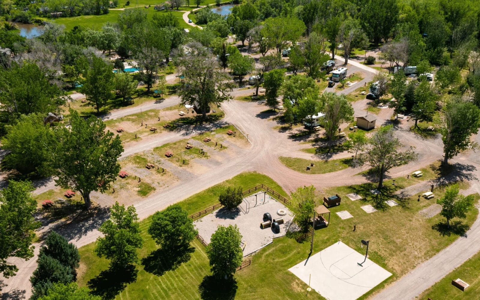 Aerial view of the Sheridan / Big Horn Mountains KOA in Wyoming with scattered tents, RVs, and trees. Roads and pathways connect various sites.