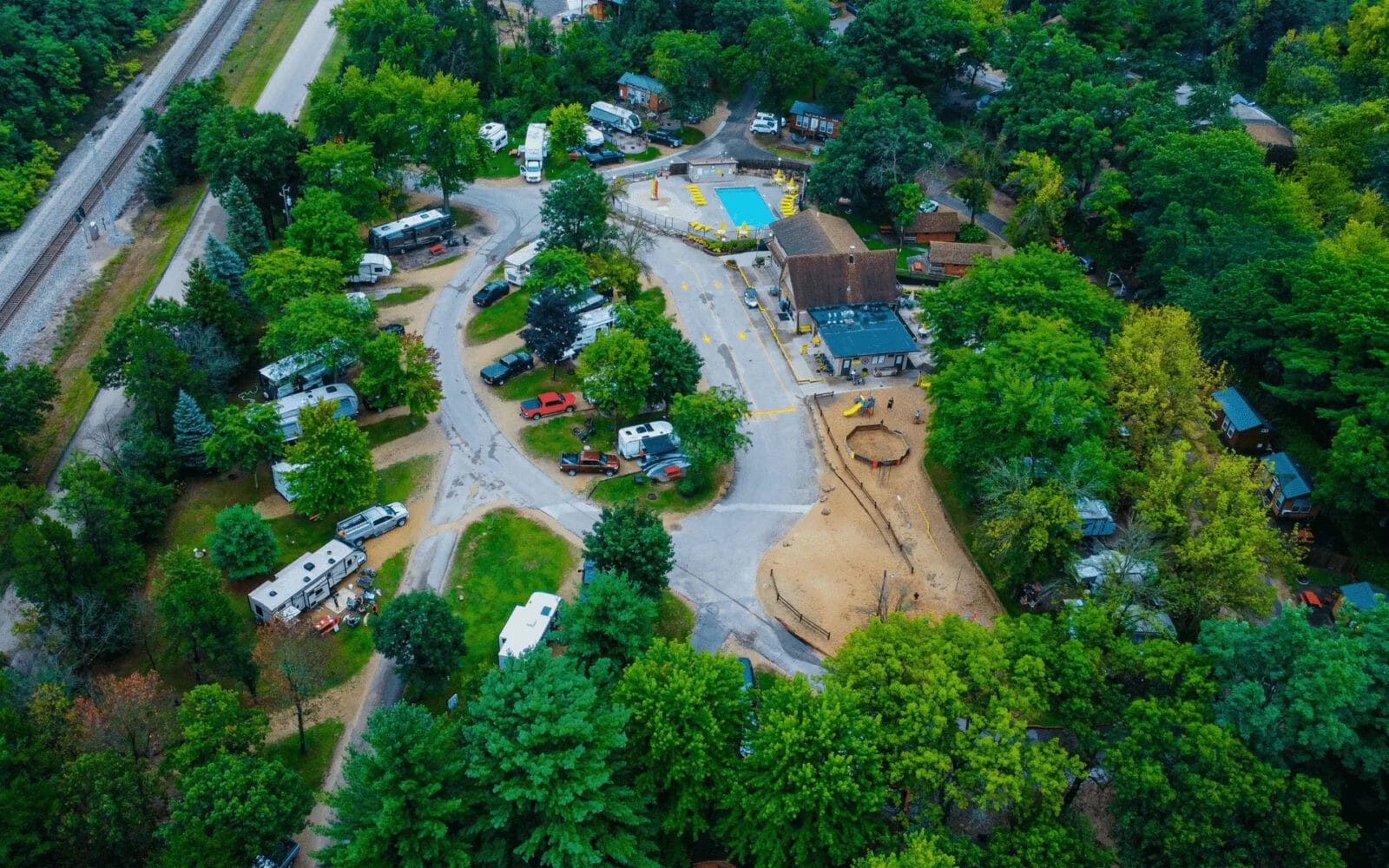 Aerial view of Wisconsin Dells KOA campground with RVs and a central building near a pool. Surrounding area is densely wooded. Roads connect various parts of the site.